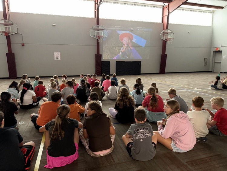 photo students setting on the floor in a gym eating ice cream and watching a movie.