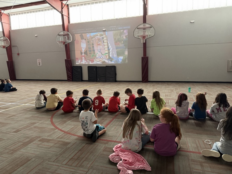 photo students setting on the floor in a gym eating ice cream and watching a movie.