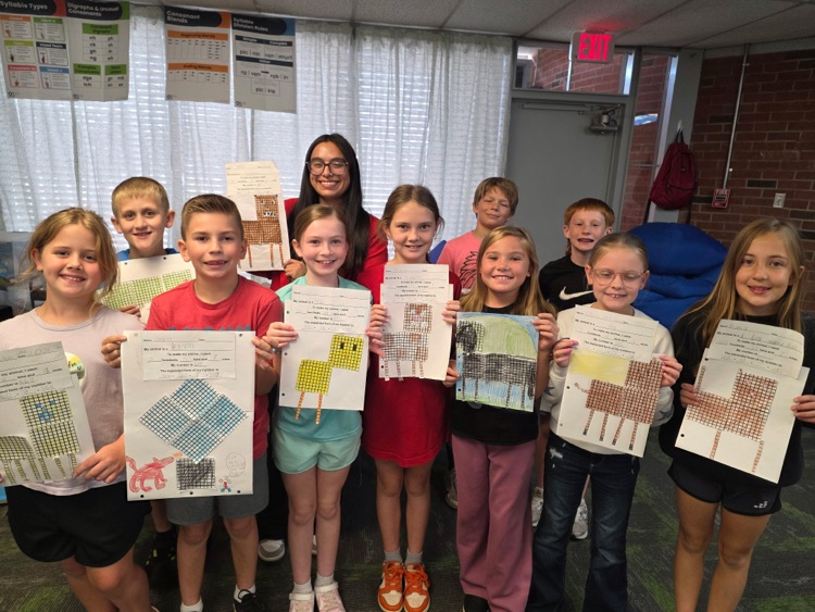 group of students standing in a classroom holding poster about place value  