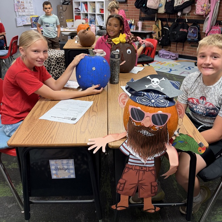 Group of students in a classroom at desks with decorated pumpkins.