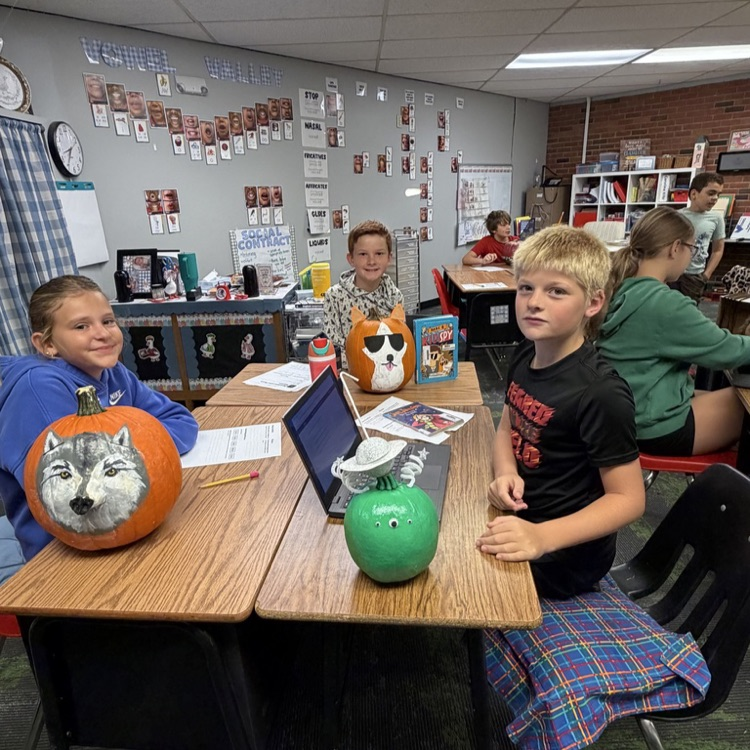 Group of students in a classroom at desks with decorated pumpkins.
