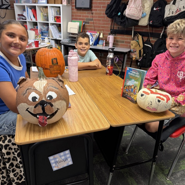 Group of students in a classroom at desks with decorated pumpkins.