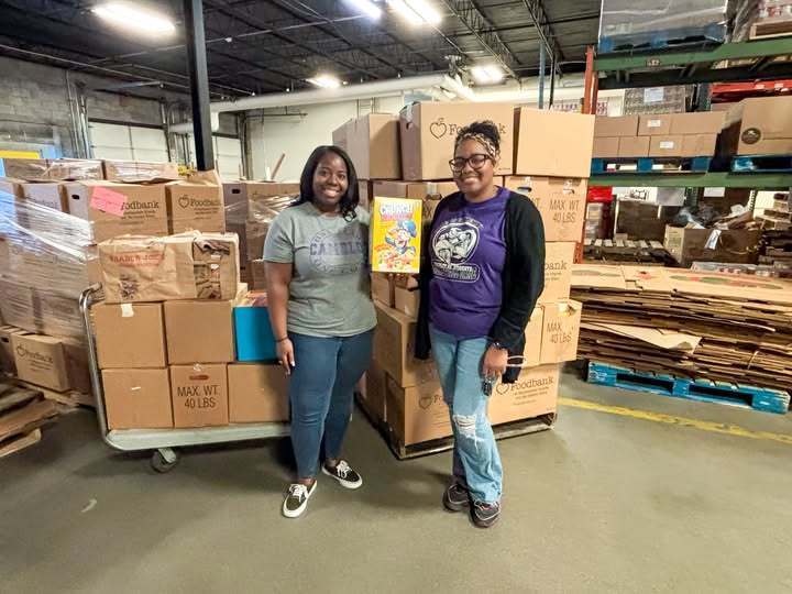two women holding a cereal box standing in front of boxes