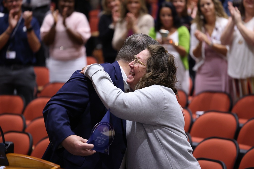 Female principal receiveing award and hugging Superindent