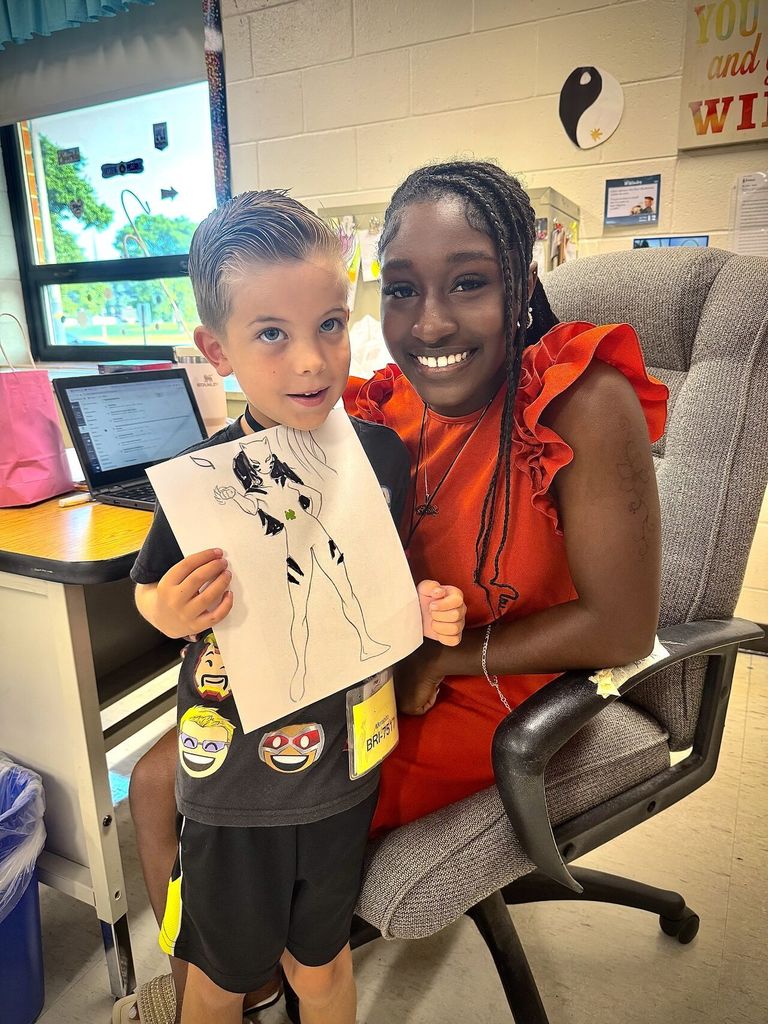 Tyanna and a student smiling with a drawing.