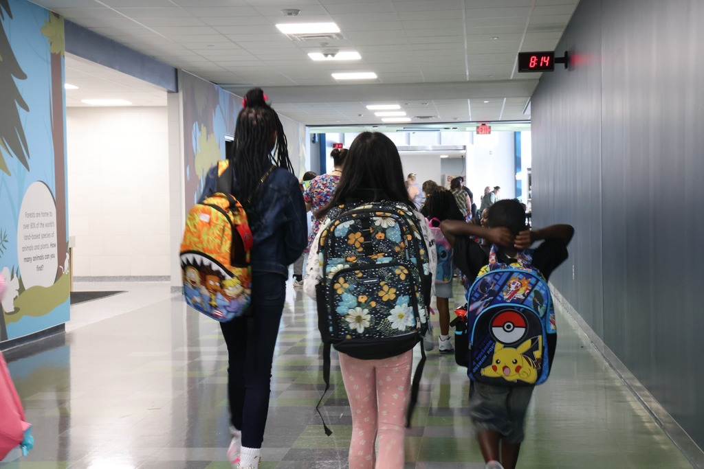 three kids walking in hall with backpacks on