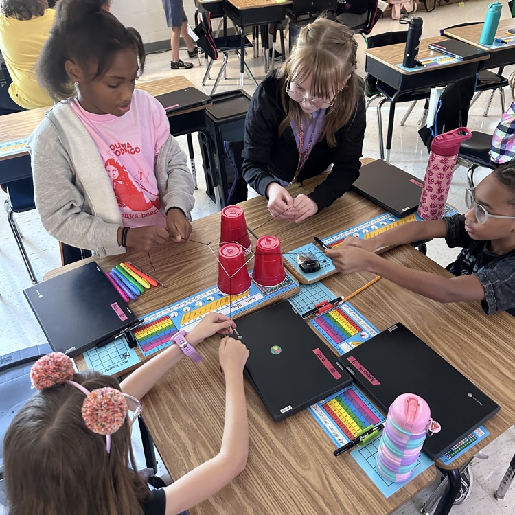 group working together with string and rubber band to stack cups 
