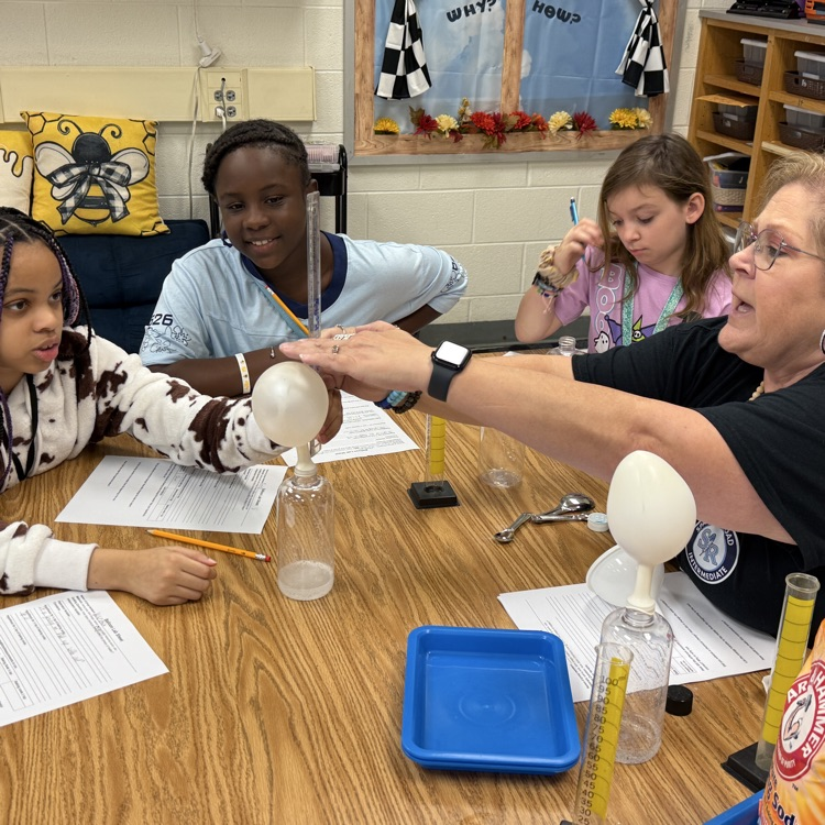 table of students and teacher with science experiment- cylinder with balloon 
