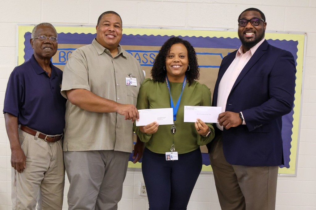 administrator holding check with 3 males on either side