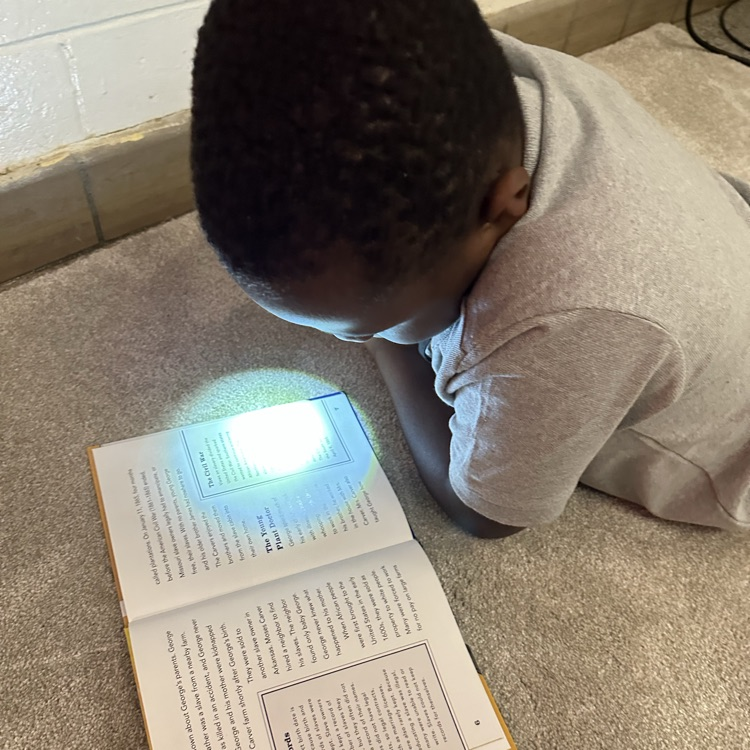 student reading with flashlight on carpet