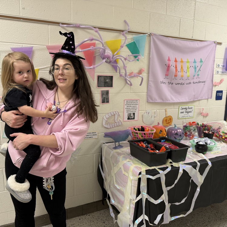 teacher with witches hat holding child by a spider themed table