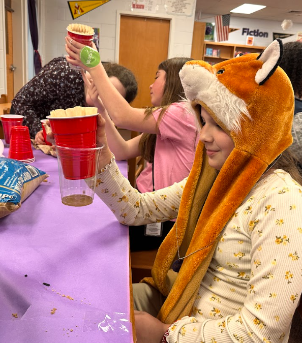 Girl is headband doing a science experiment with a red solo cup.
