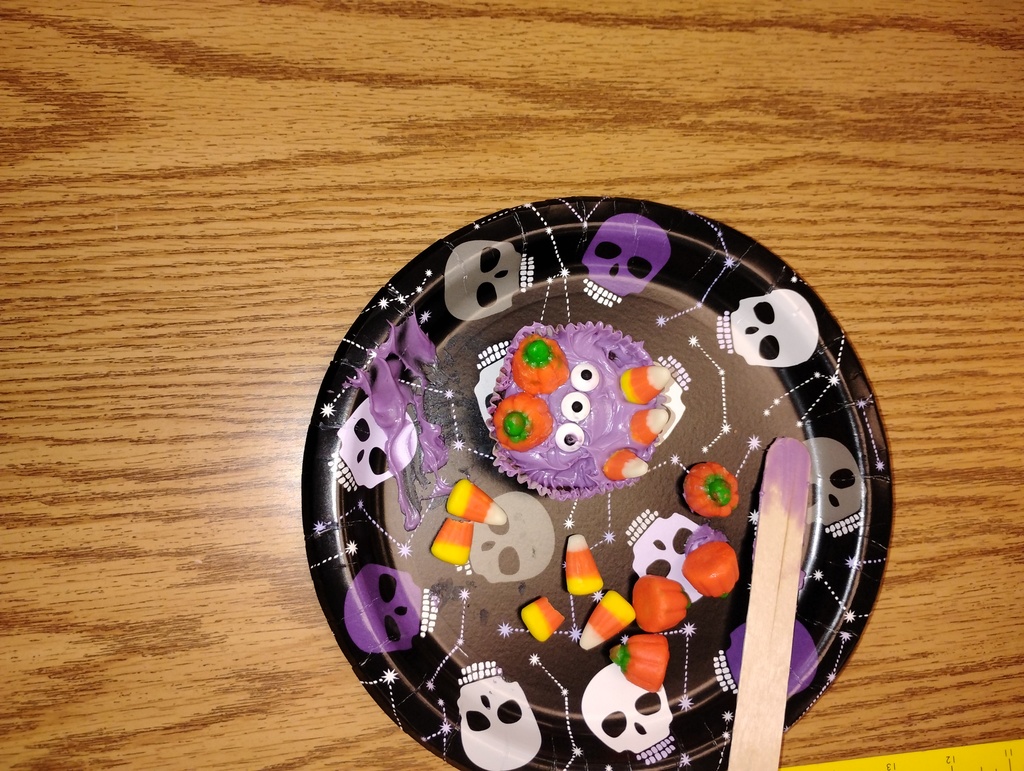 Cupcake montster with purple icing, decorated with candy pumpkins, candy corn, and candy eyeballs
