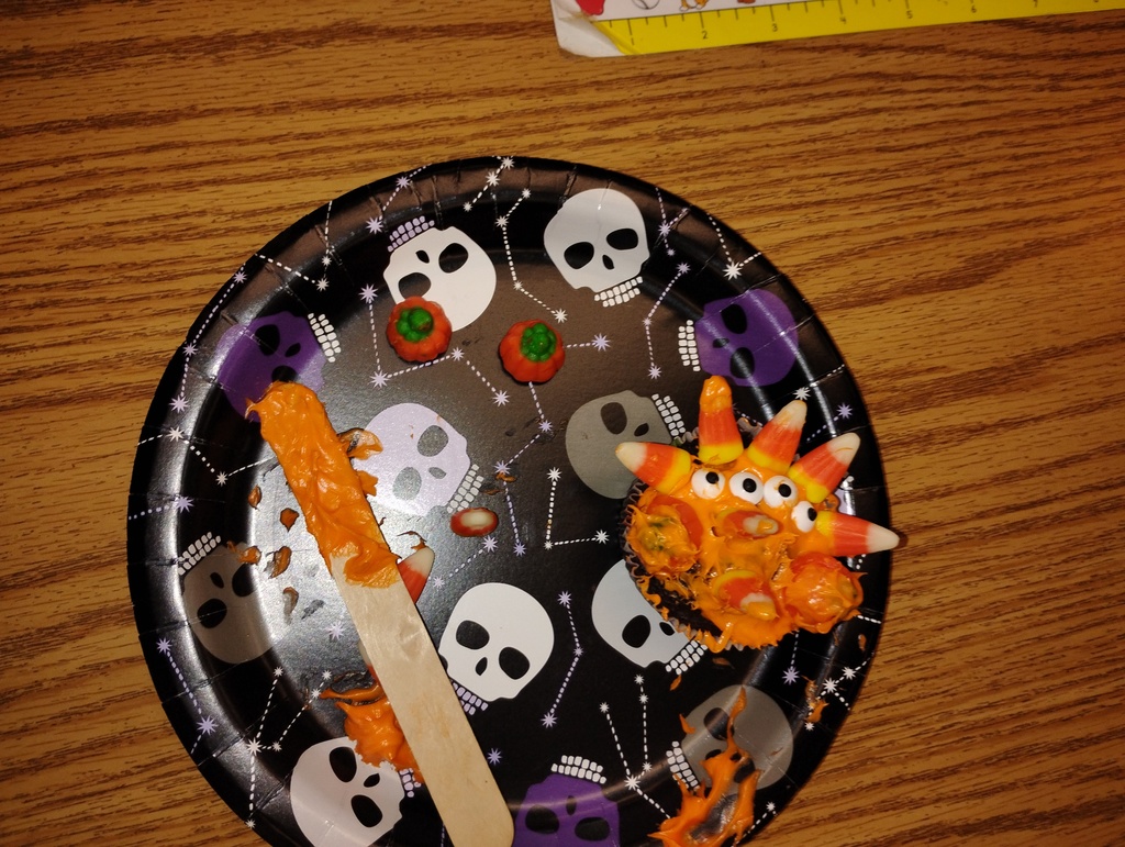 Cupcake montster with orange icing, decorated with candy pumpkins, candy corn, and candy eyeballs