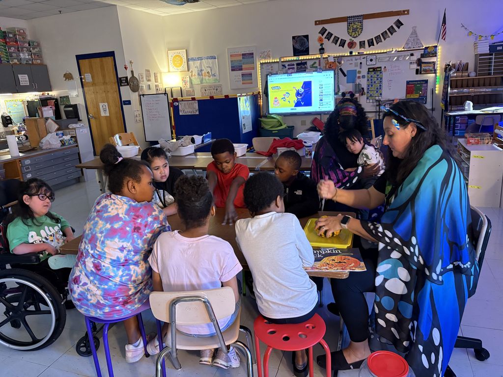 Mrs. Yohe carves the pumpkin while students watch