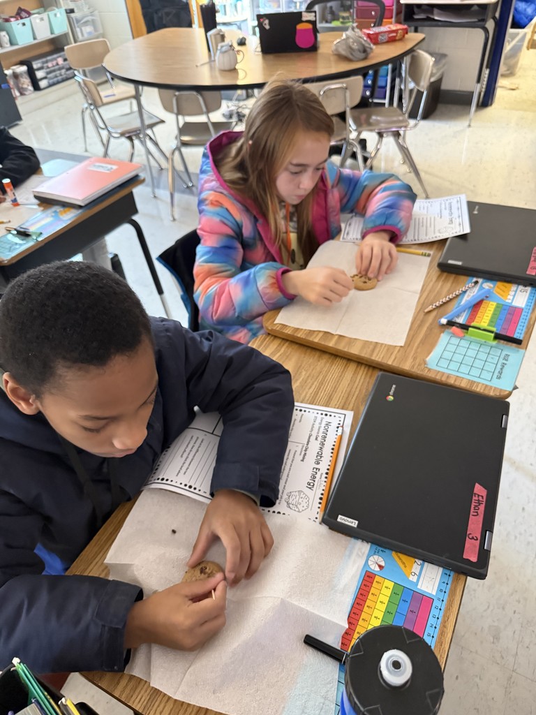 Two students at their desk with toothpicks trying to remove the chocolate chips.
