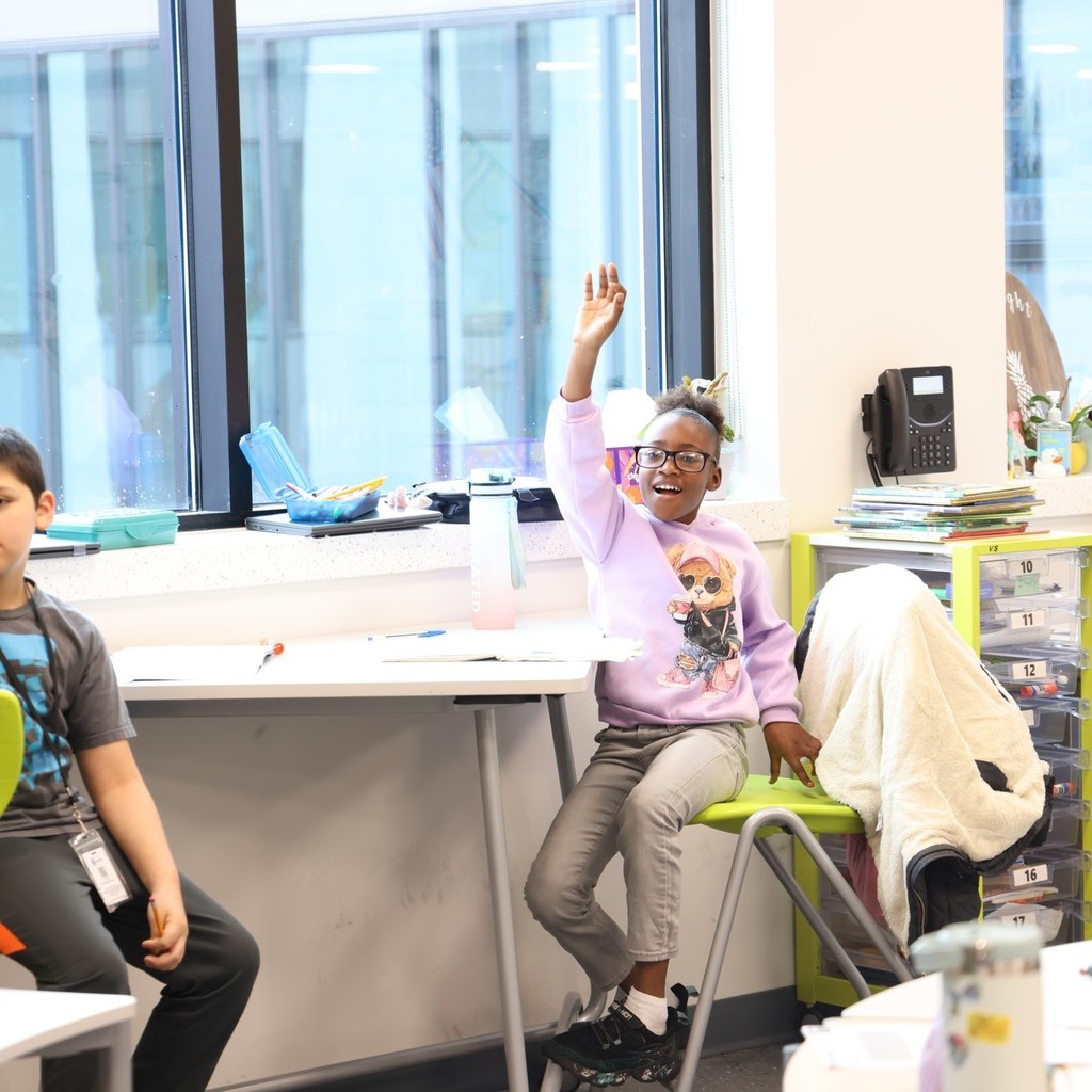 Student smiling and raising her hand to participate.