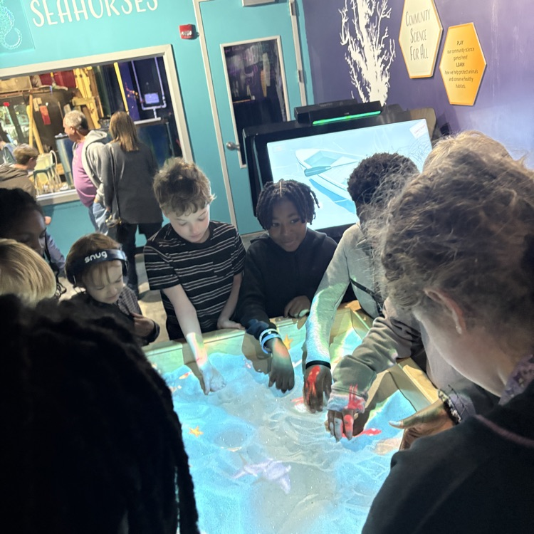 students around a sand table with projector 