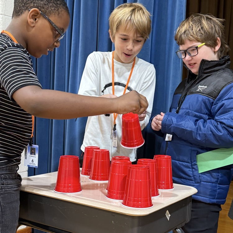 together we rise challenge three students work together to stack cups 