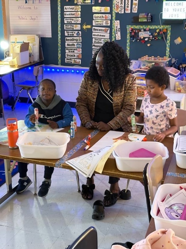 teacher helps students creating colorful fall trees with hand trunks and bingo marker leaves