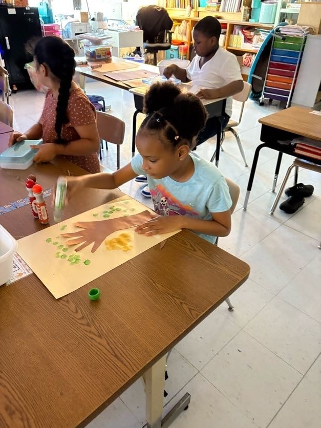 students creating colorful fall trees with hand trunks and bingo marker leaves