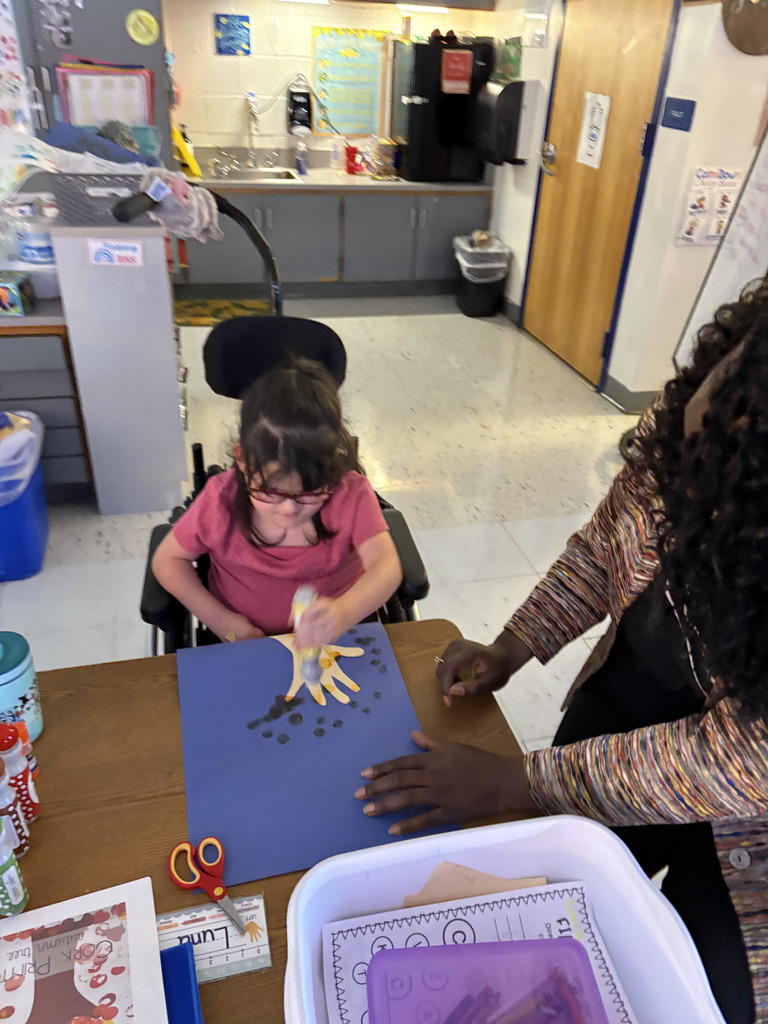 teacher helps student creating colorful fall trees with hand trunks and bingo marker leaves