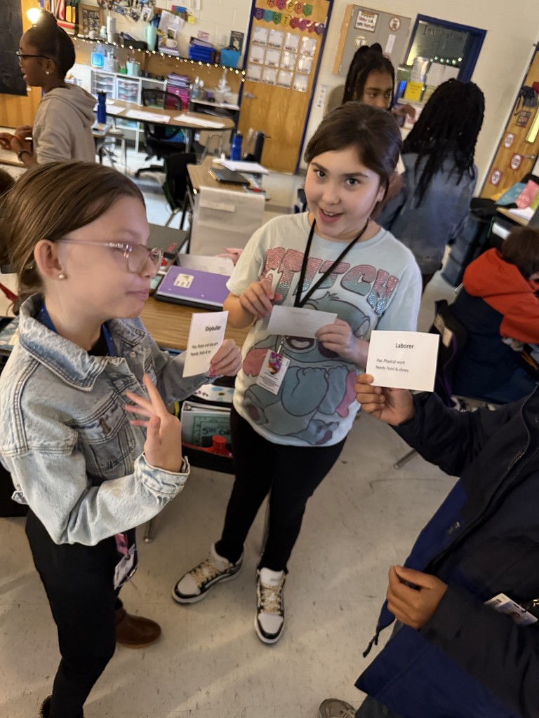 Students holding cards in a circle trying to barter for goods.