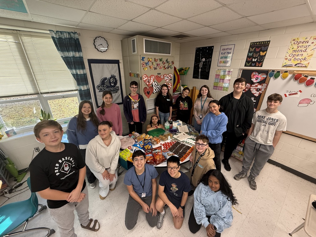 students in a classroom gathered around a table of goodies to share