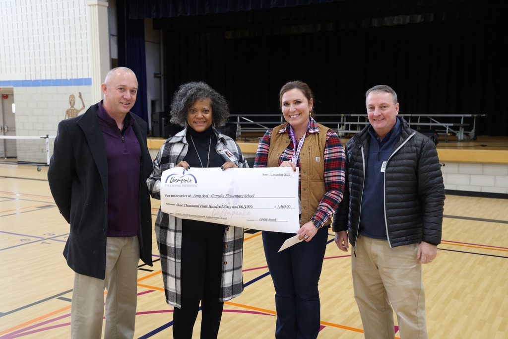 two ladies holding a giant grant check while 2 men stand on either side of them in a gym