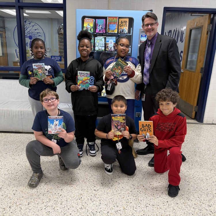 students holding books in front of book vending machine with Mr. Triolet