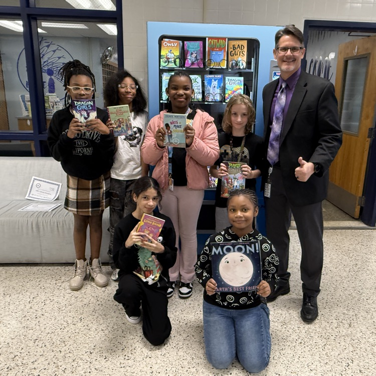 students holding books in front of book vending machine with Mr. Triolet