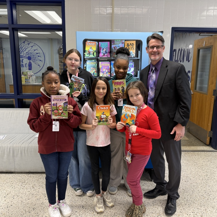 students holding books in front of book vending machine with Mr. Triolet