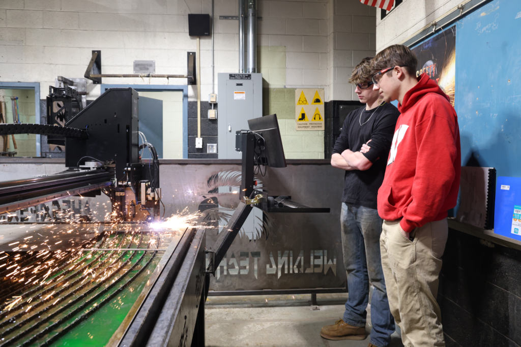 two male CCC students observing welding equipment in use and sparks flying