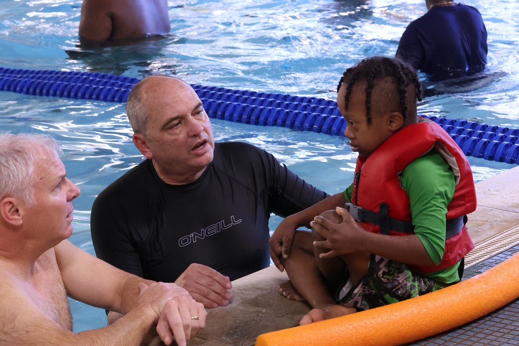 Two teachers in the pool talking to a primary students who is sitting on the side