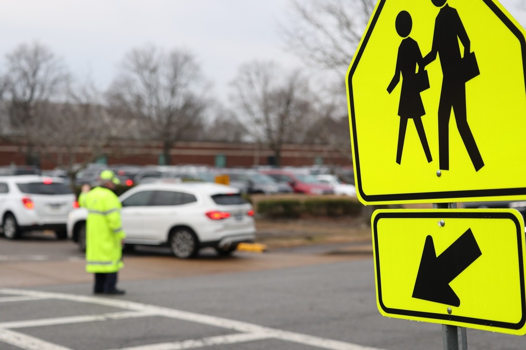 Crossing sign with blurry Mr. Compton in background directing traffic