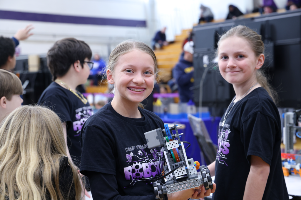 two middle school girls smiling for camera with robot in hand