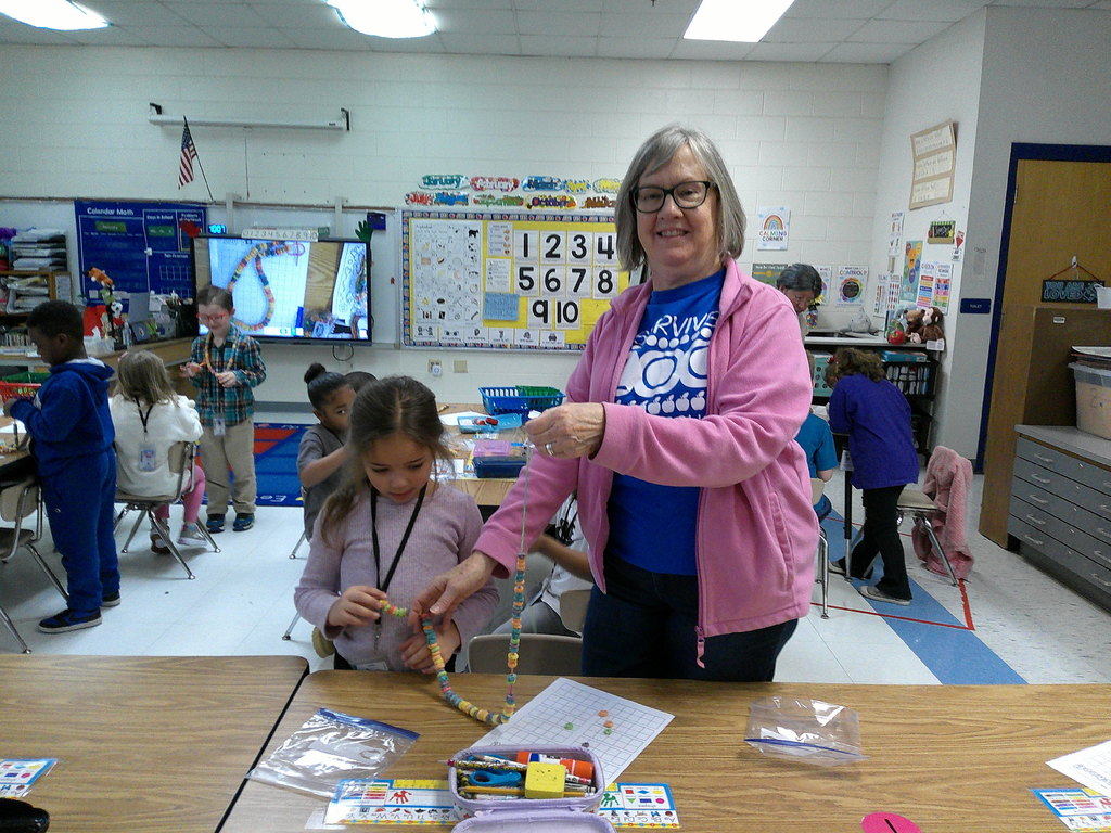 Mrs. Daniel helps a student with her 100th day necklace