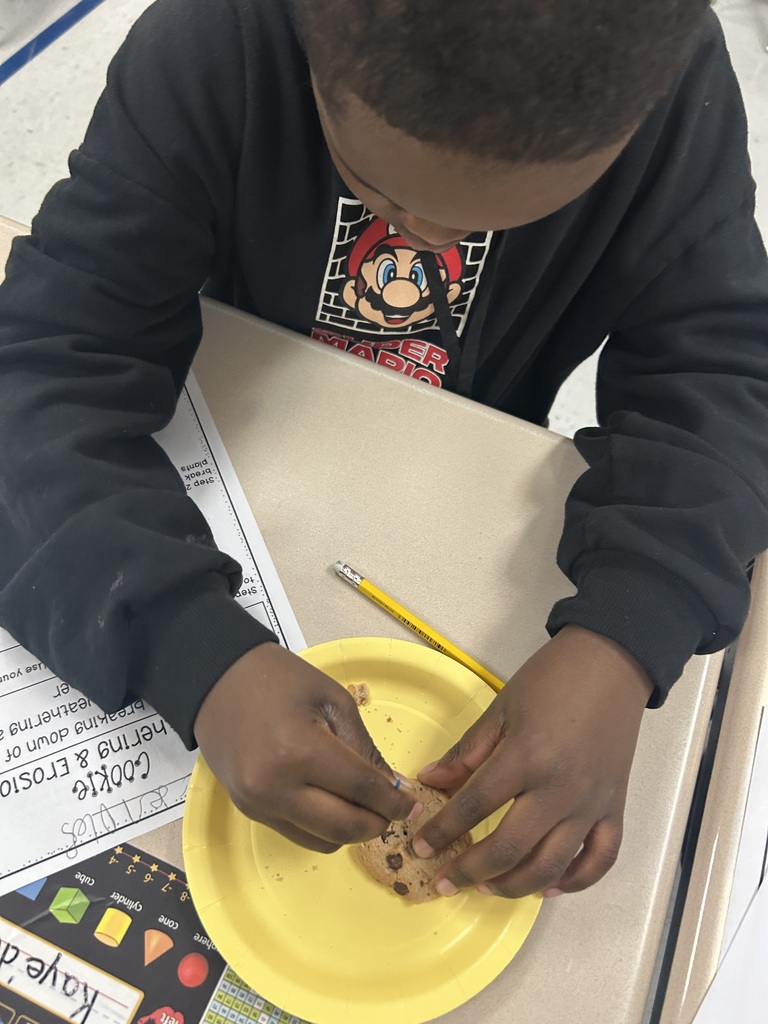 A close up of a second grade student mimicking the effects of erosion using a toothpick on a chocolate chip cookie