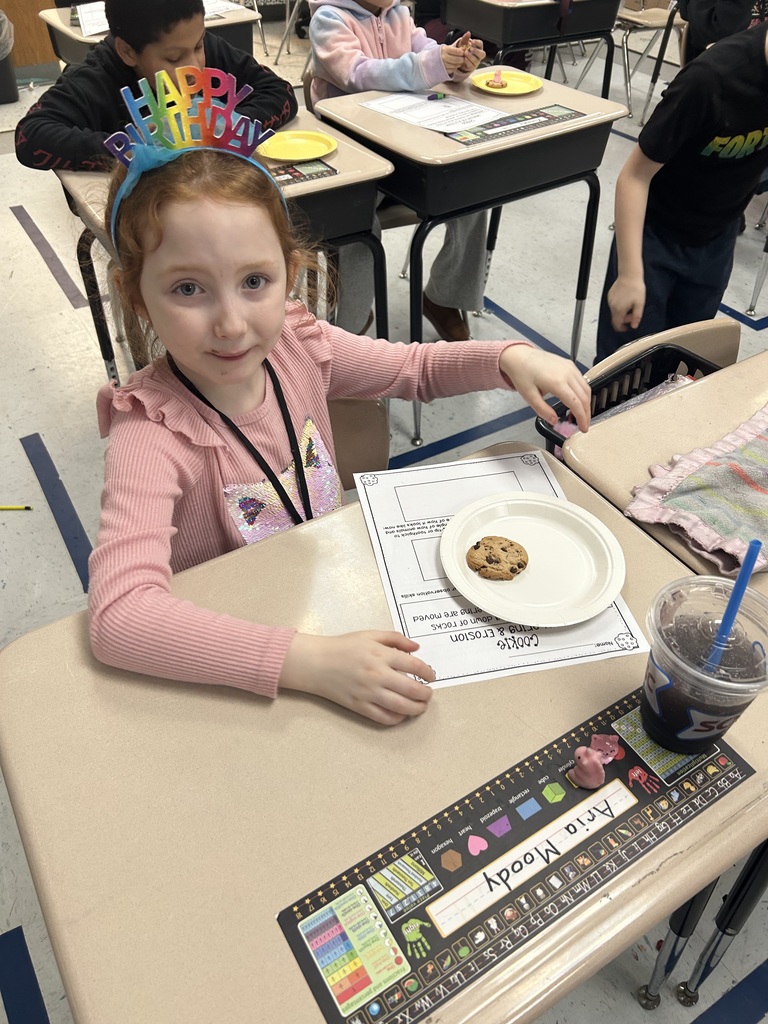 A student smiling at the camera with her cookie sitting on the desk for the erosion experiment