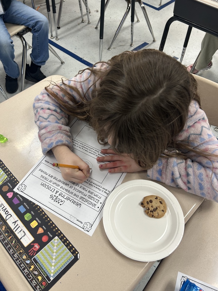 A close up of a second grade student recording her observations of the effects of erosion on a chocolate chip cookie