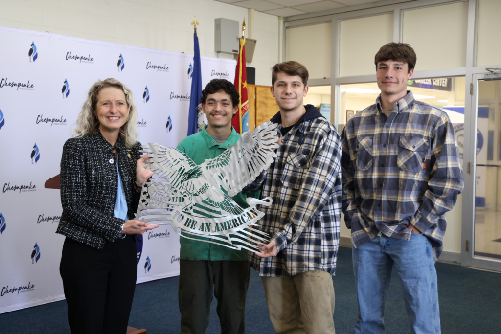 3 welding students presenting Kiggins with metal eagle cut out.