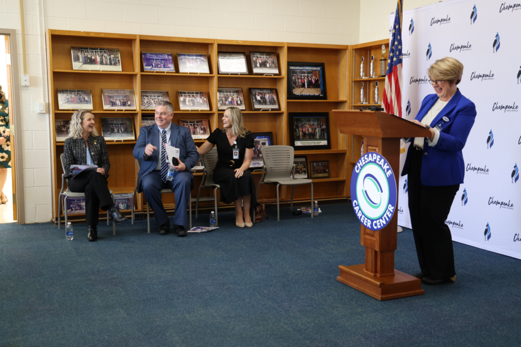 Dr. kitchens at podium whil school leaders and Kiggins sit smiling on the side