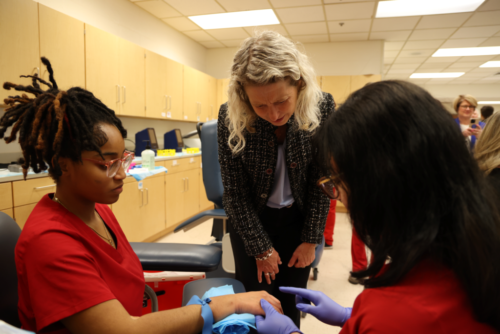 Jen kiggins standing over two students who are getting ready for a blood draw