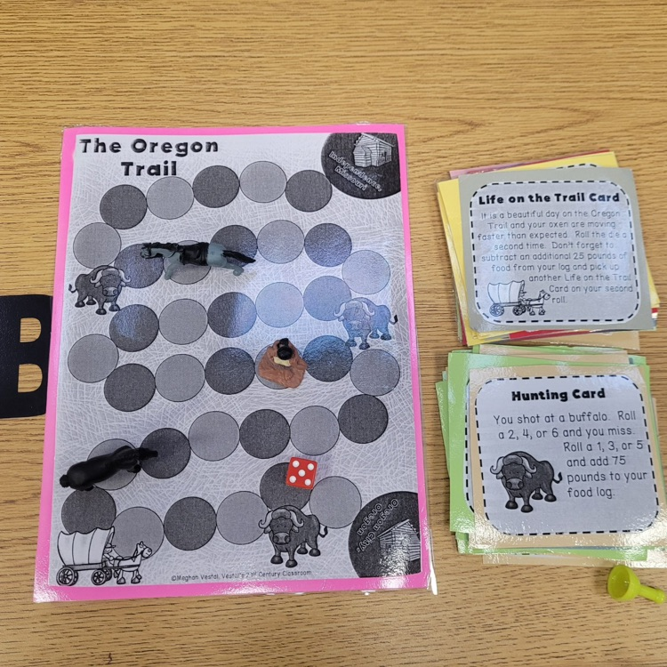 Students sit at desks in a classroom playing a paper-based version of the Oregon Trail game, using worksheets and materials to make decisions and track their journey while learning about westward expansion.