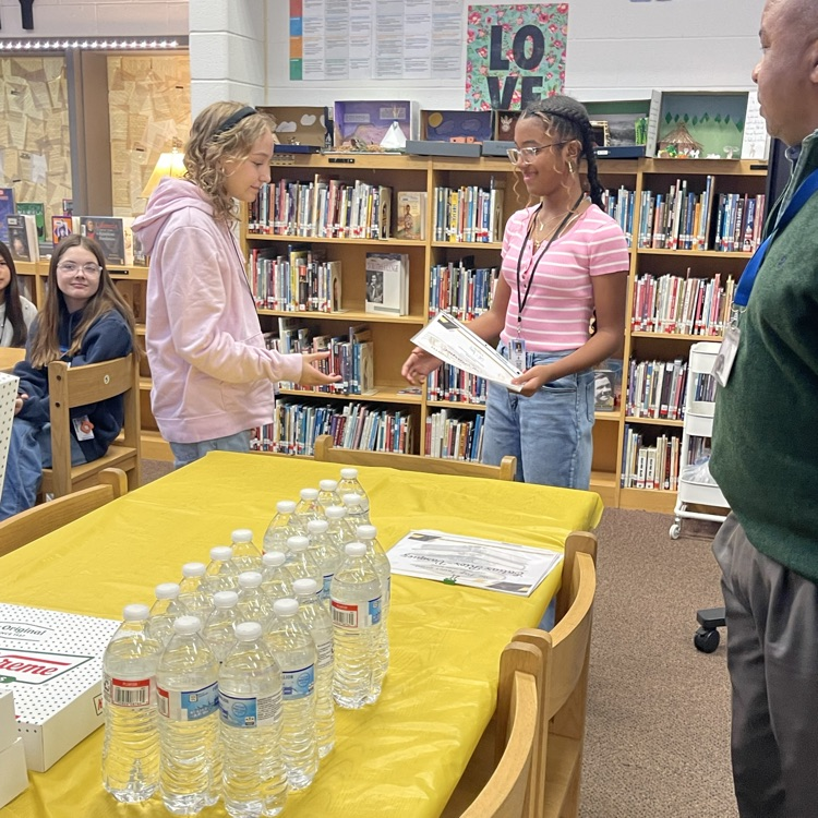 Students celebrating at a Scholar of the Month breakfast, posing with donuts in front of a commemorative banner.