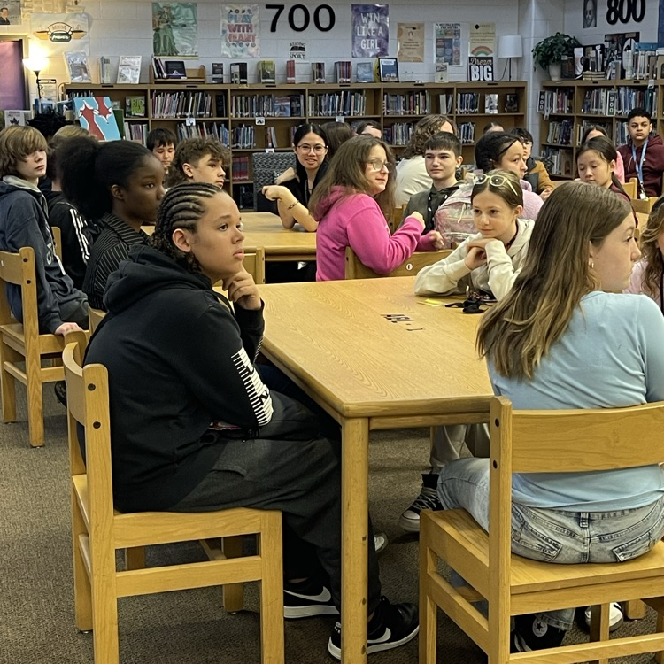 Students celebrating at a Scholar of the Month breakfast, posing with donuts in front of a commemorative banner.