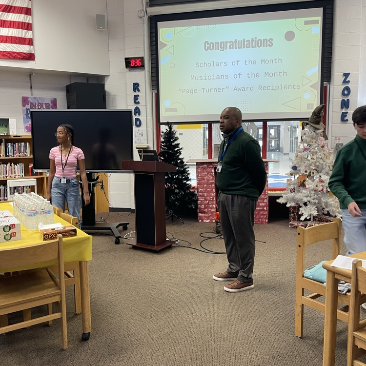 Students celebrating at a Scholar of the Month breakfast, posing with donuts in front of a commemorative banner.