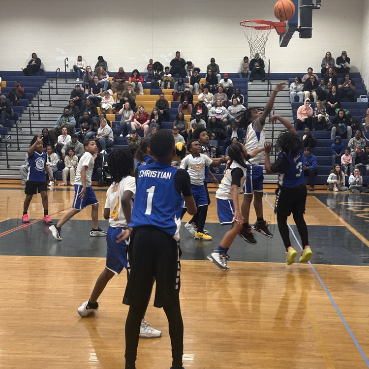 Basketball players on the court taking a shot and another player blocking 