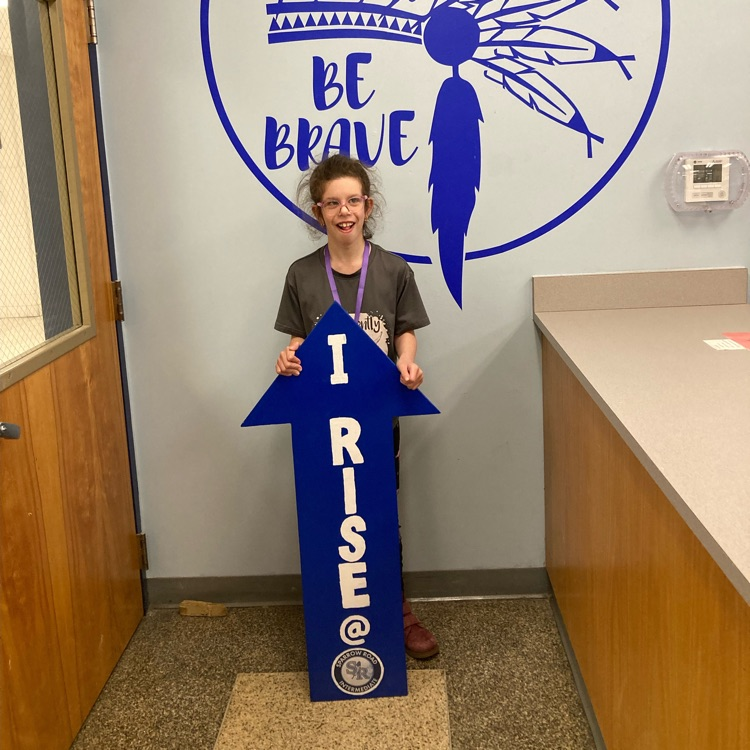 student proudly standing by the  I RISE arrow. 