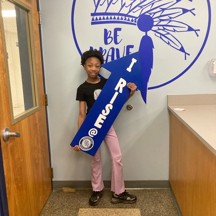 student proudly holding the I RISE arrow. 